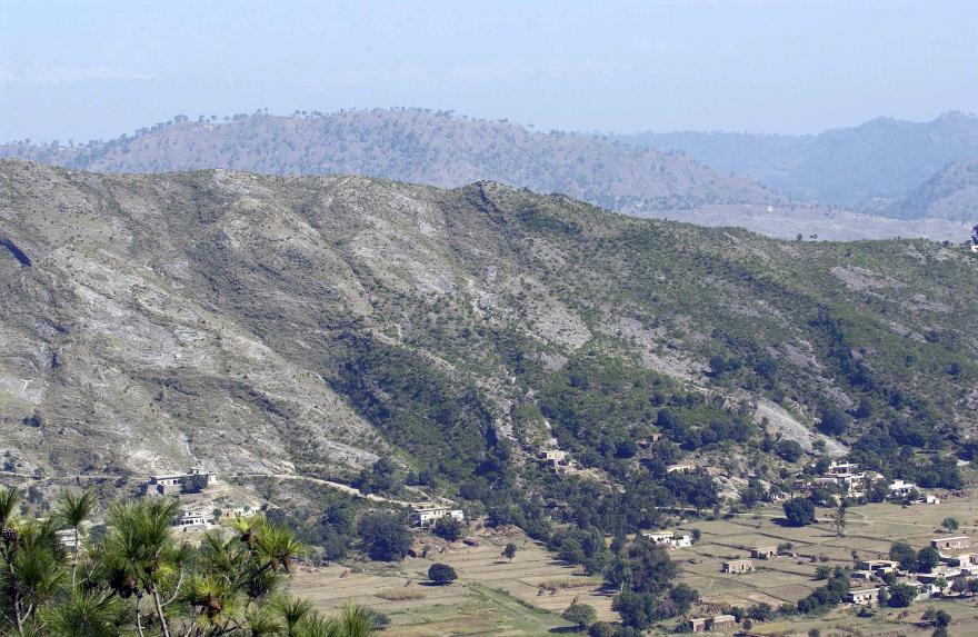 Mountainous terrain with scattered trees and small villages in valleys, under a clear blue sky.